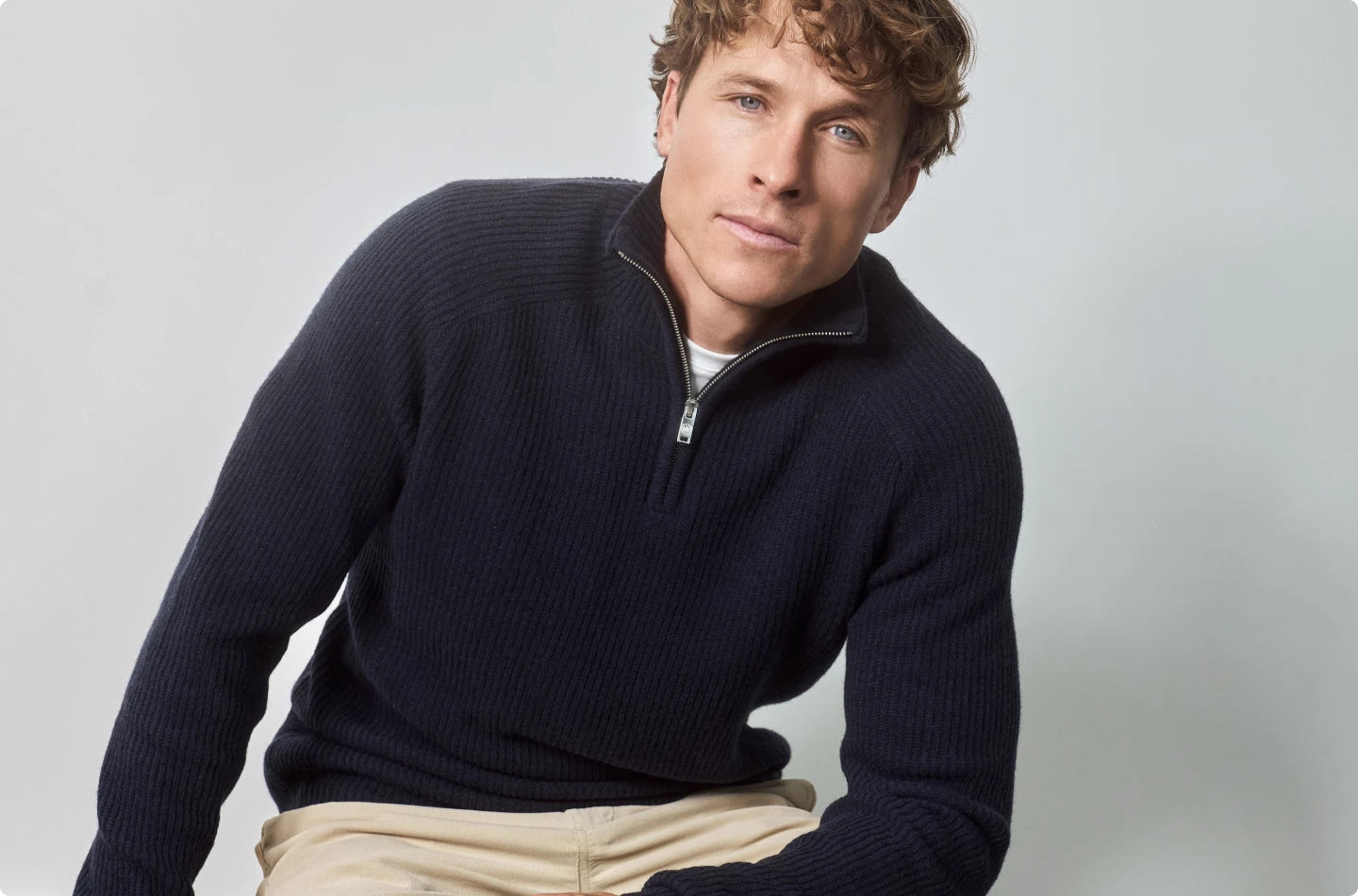 Dunkelblauer Strickpullover von KRONSTADT mit hohem Kragen und Half-Zip, getragen von blondem Model vor hellgrauem Hintergrund