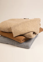 Gestapelte Strickpullover von KRONSTADT in Hellgrau, Camelbraun und Beige, vor beigem Hintergrund