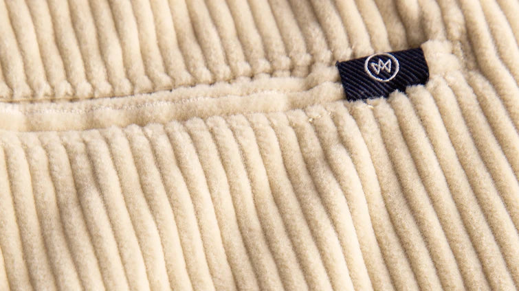 Detailaufnahme von beigem Cordstoff mit schwarzem Logo-Patch und hellem Kronen-Logo von KRONSTADT